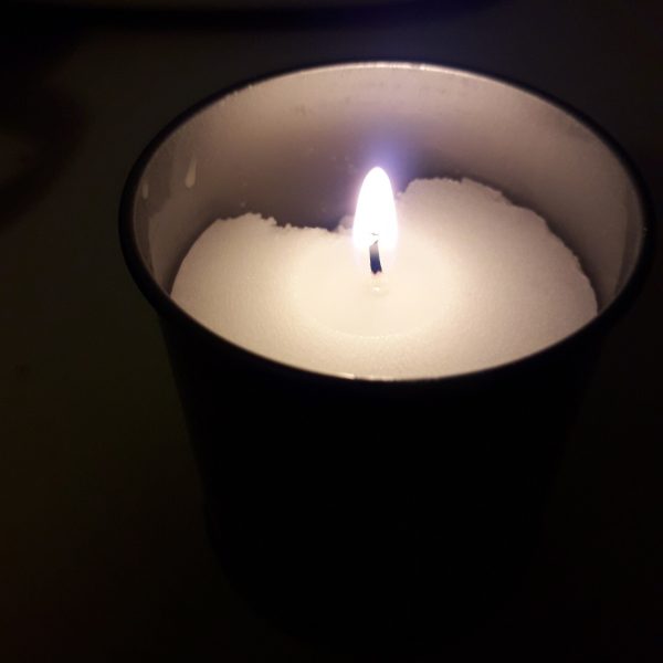 شمعة بيضاء مشتعلة في كوب زجاجي داكن